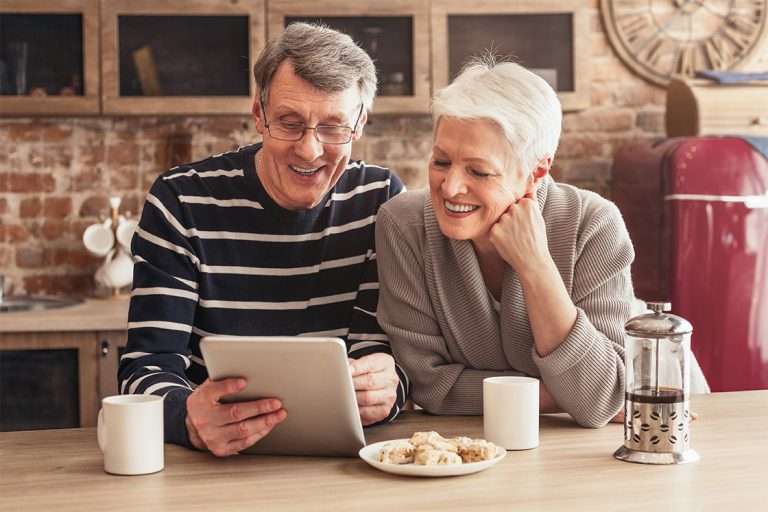 happy senior couple are sitting their kitchen looking tablet computer woman has hand