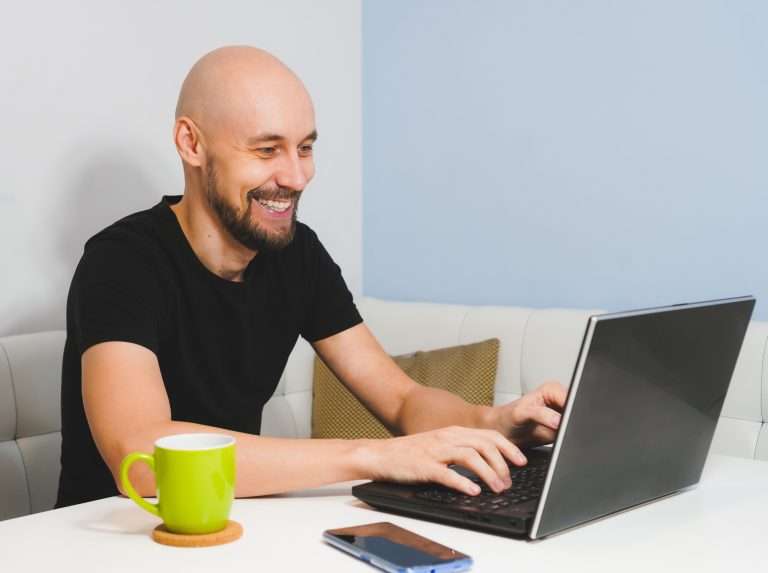 smiling bald man with beard black tshirt working his notebook home side view